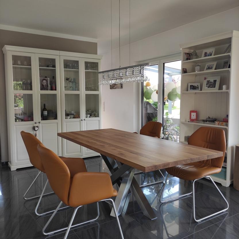 Stilvolles Esszimmer mit maßgefertigtem Holztisch auf Metallgestell, umgeben von Vitrinenschränken und Ledersesseln, ideal für eine elegante und gemütliche Atmosphäre.