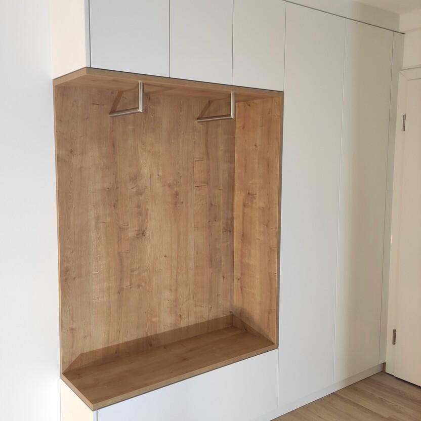 Moderne Garderobe nach Maß mit weißen Schrankfronten, hölzerner Rückwand und integrierter Sitzfläche, perfekt für eine stilvolle und funktionale Flureinrichtung.