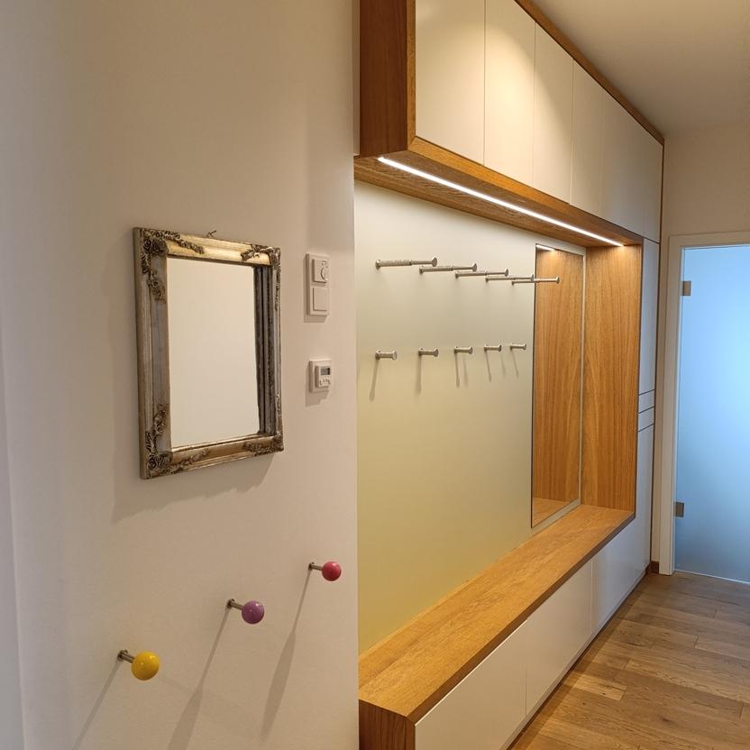Stilvolle Flurgarderobe nach Maß mit hölzernen Akzenten, weißen Schrankfronten, integrierter Beleuchtung und praktischen Kleiderhaken, ideal für eine elegante und funktionale Flurgestaltung.