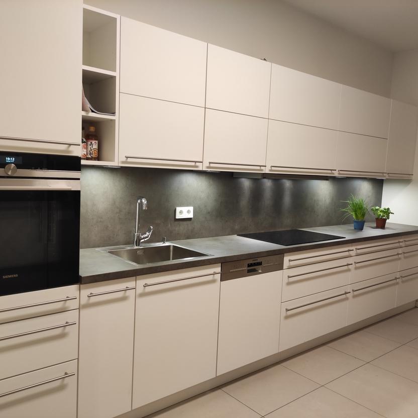 Moderne Einbauküche nach Maß mit weißen Fronten, dunkler Arbeitsplatte, integriertem Backofen und Spüle, sowie stilvoller Beleuchtung für eine hochwertige Küchenausstattung.