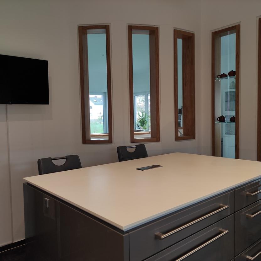 Moderne Kücheninsel mit Hochglanzfronten, großer weißer Arbeitsfläche und integriertem Stauraum, ergänzt durch Holzfensterrahmen und Wand-TV für eine stilvolle Küchengestaltung.