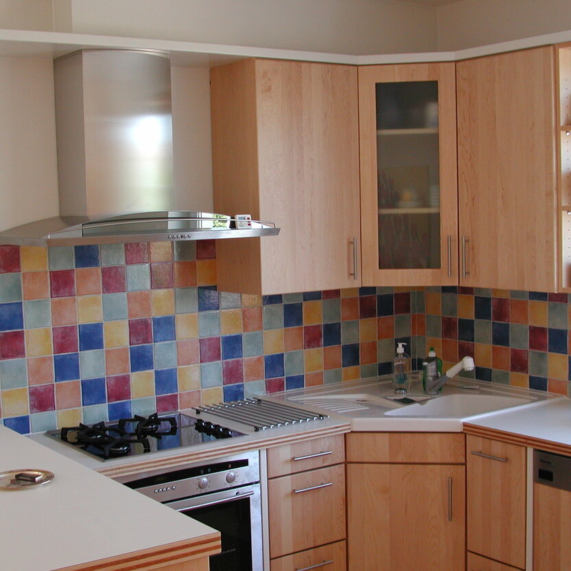 Maßgefertigte Eckküche mit Holzfronten, buntem Fliesenspiegel und moderner Ausstattung, ideal für eine lebendige und funktionale Küchengestaltung.