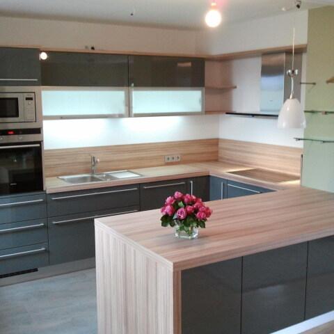 Moderne Küche mit hochglänzenden grauen Fronten, Holzarbeitsplatte und Kücheninsel, ausgestattet mit hochwertigen Geräten für eine stilvolle und praktische Küchengestaltung.