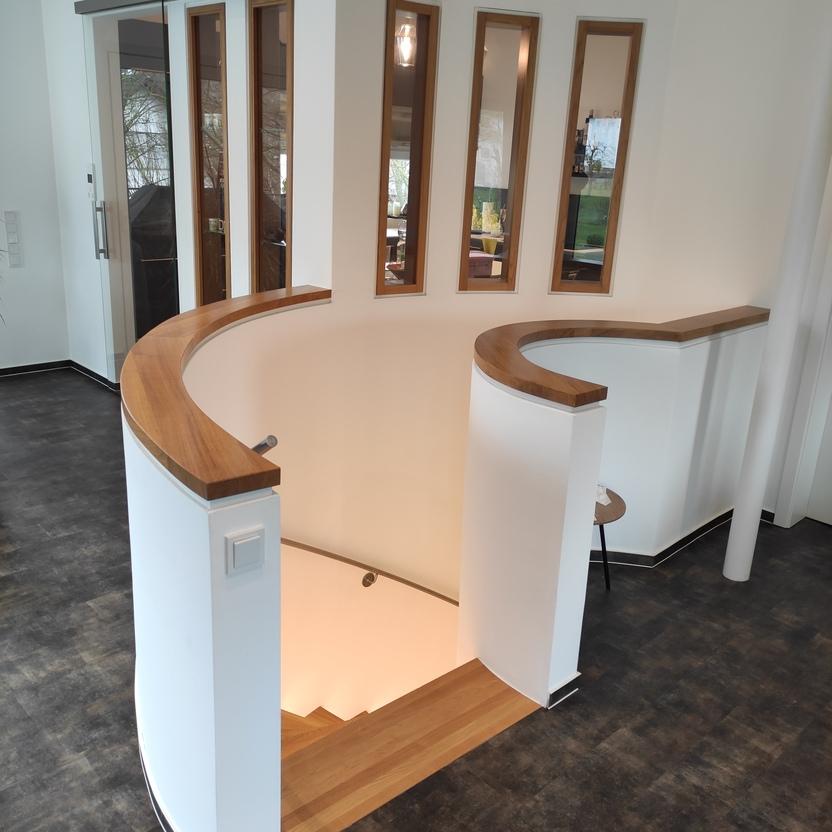 Rundes Treppengeländer aus Holz und weißem Material, harmonisch in die Wohnraumgestaltung integriert, ideal für eine moderne und elegante Atmosphäre.