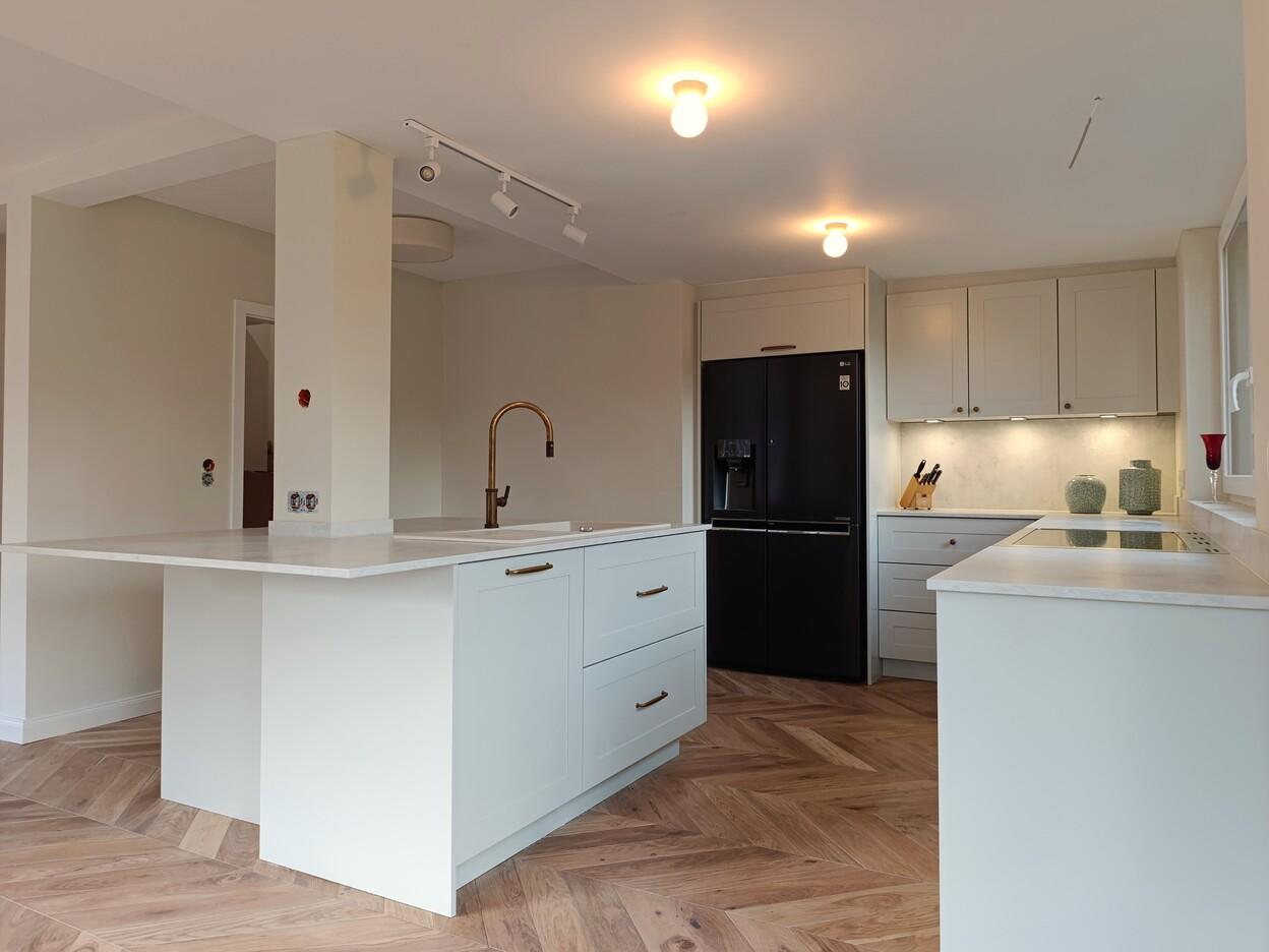 Moderne Küche nach Maß mit heller Kücheninsel, Einbauküchenschränken und schwarzem Kühlschrank – gefertigt in Handarbeit für Kunden im Raum Kassel.