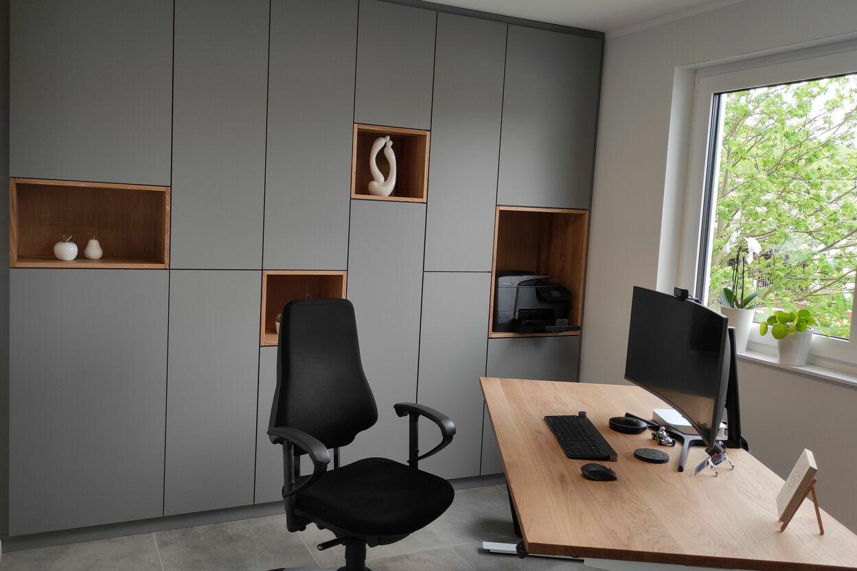 Modernes Büro mit maßgefertigten grauen Schränken, offenen Holzfächern und einem hochwertigen Schreibtisch aus Holz, perfekt für eine funktionale und stilvolle Arbeitsumgebung.