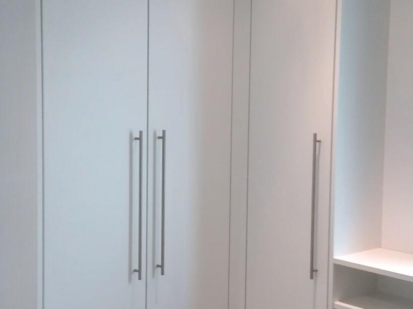 Funktionaler Eckschrank nach Maß in modernem Weiß mit schlichten Edelstahlgriffen und integriertem Regalfach, ideal für die platzsparende Einrichtung von Fluren.
