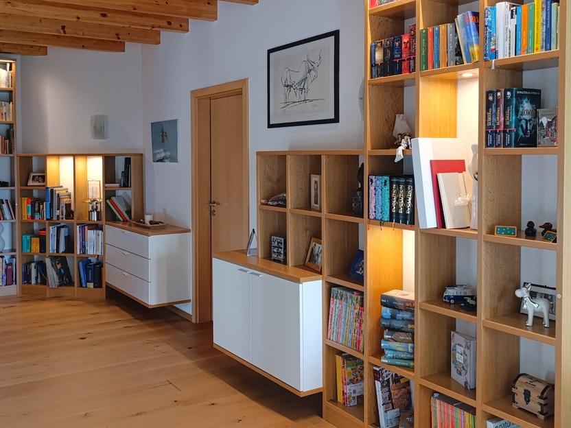 Stilvolle Bücherregale aus Holz mit integrierter Beleuchtung und weißen Schubladenelementen, perfekt für eine moderne und elegante Wohnraumgestaltung.