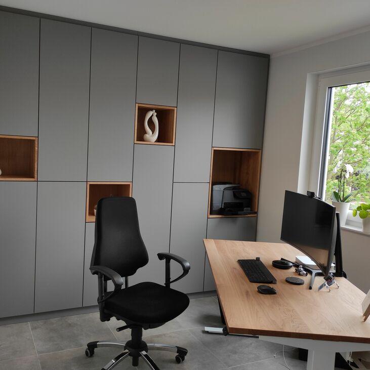 Modernes Büro mit maßgefertigten grauen Schränken, offenen Holzfächern und einem hochwertigen Schreibtisch aus Holz, perfekt für eine funktionale und stilvolle Arbeitsumgebung.