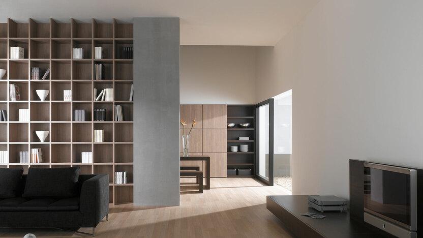 Offene Wohnraumimpression mit Einbauregal für Bücher und Dekoration in Trennwand mit hellem Holzboden