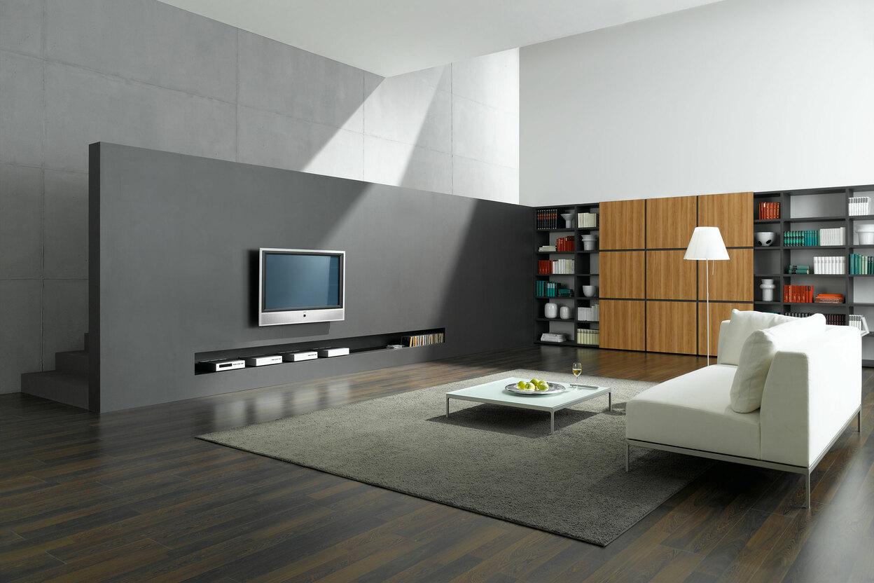 Offene Wohnraumimpression mit grauer TV-Trennwand zur Treppe und Einbauregal aus Holz und weißem Sofa